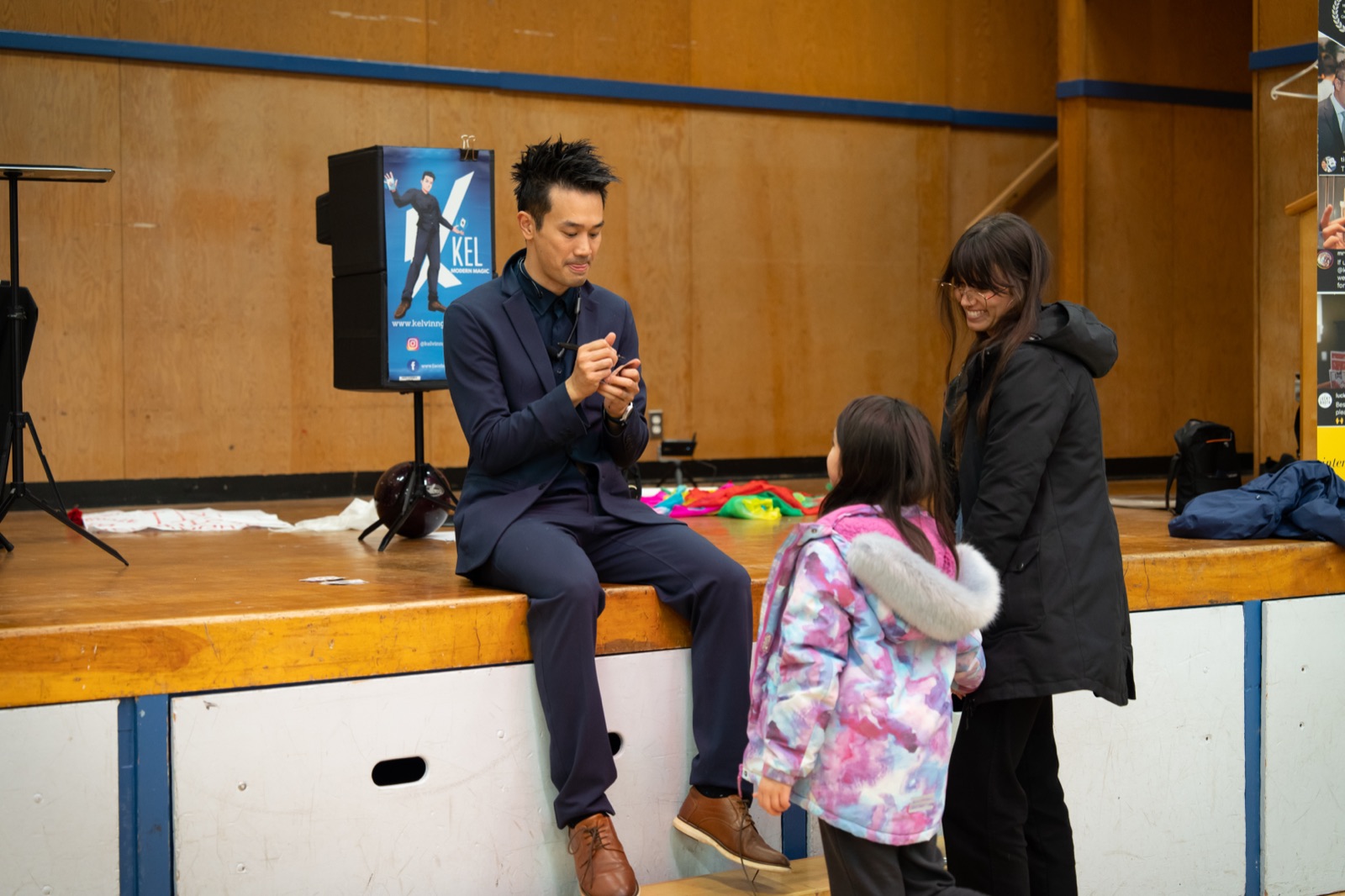 Kel performing close-up magic with a student volunteer on stage at the Connaught Heights PAC fundraiser show