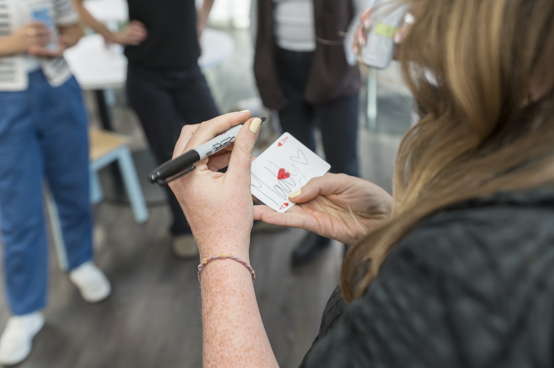 A guest signing the face of a playing card with a marker during close-up magic at a Vancouver corporate happy hour