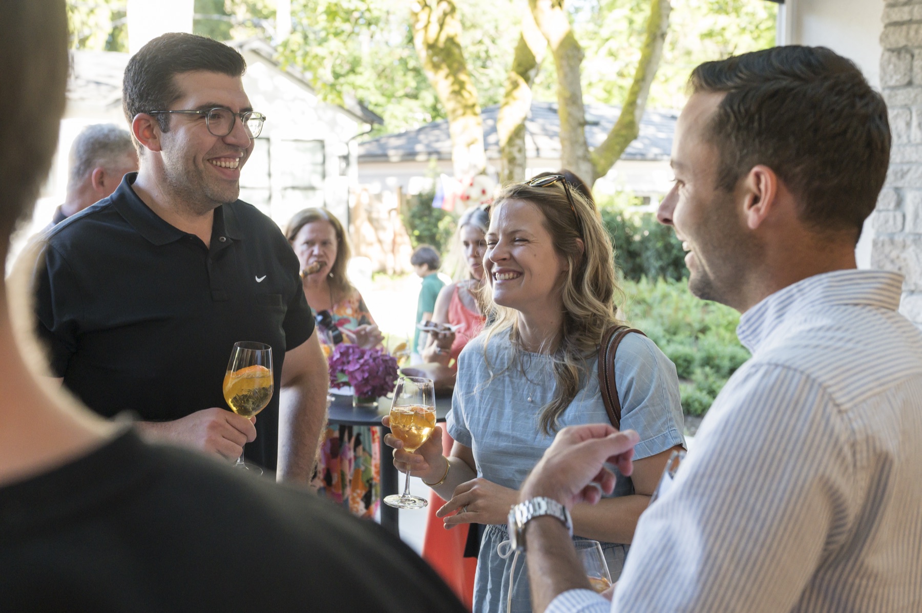 Three guests laughing together with drinks in hand during the garden reception at a Vancouver corporate summer party