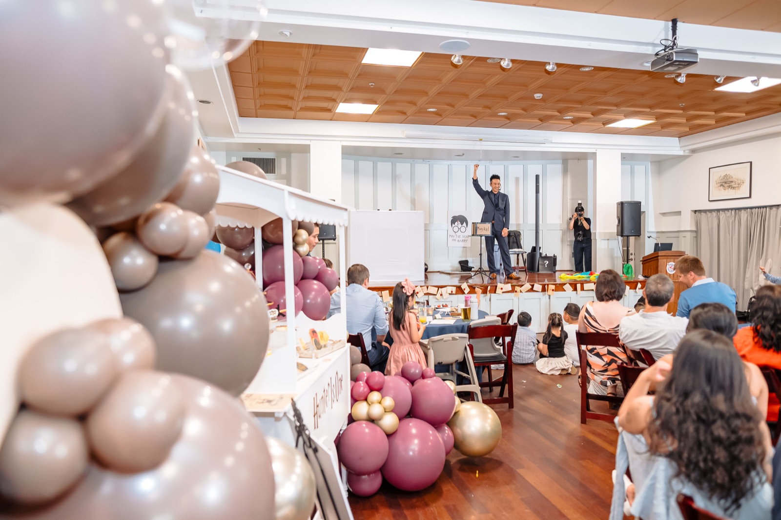 Guests watching a magic show in front of a mauve and gold balloon installation at a Vancouver first birthday