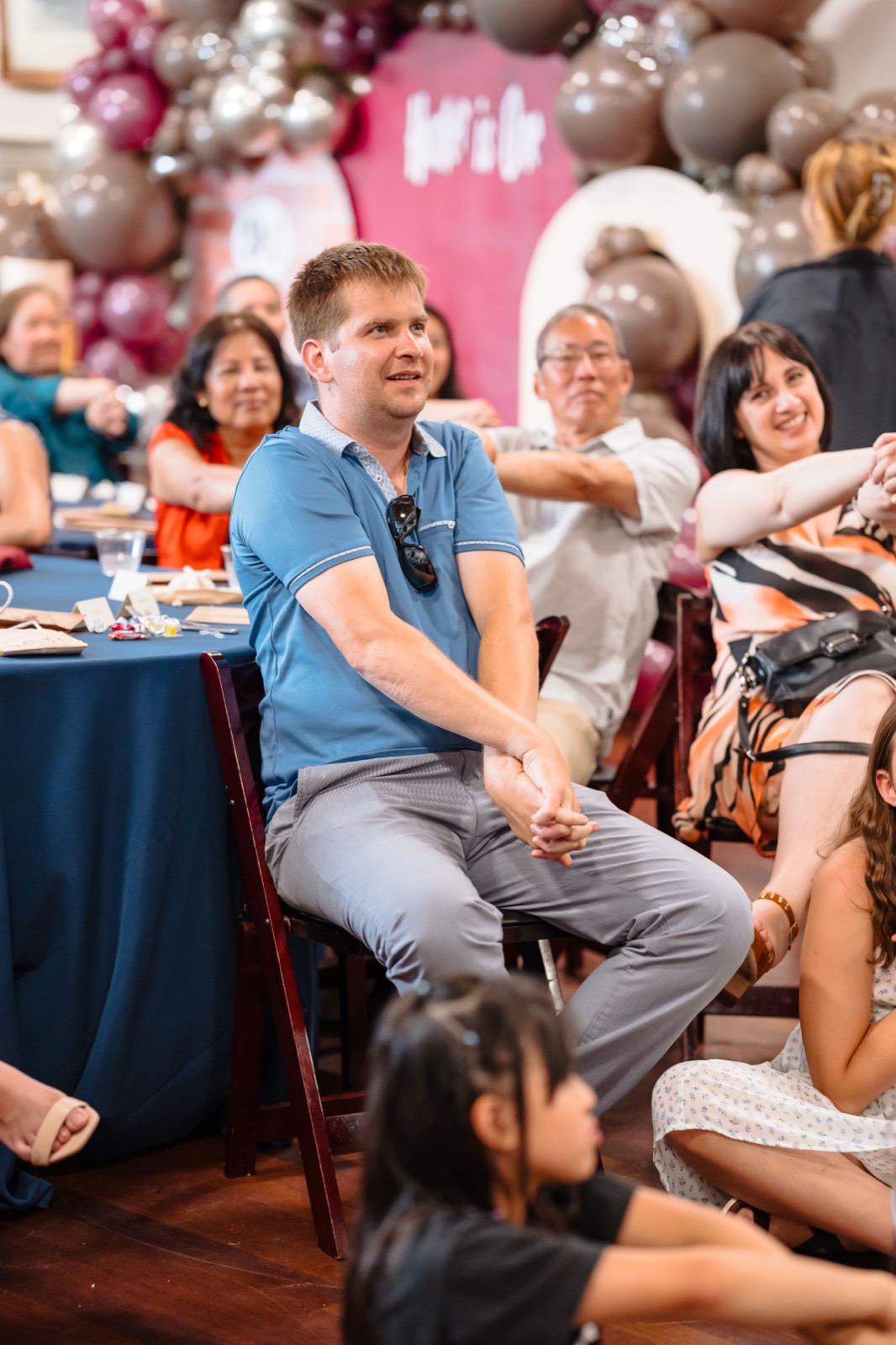 Party guests laughing during a magic show with a balloon garland backdrop behind them
