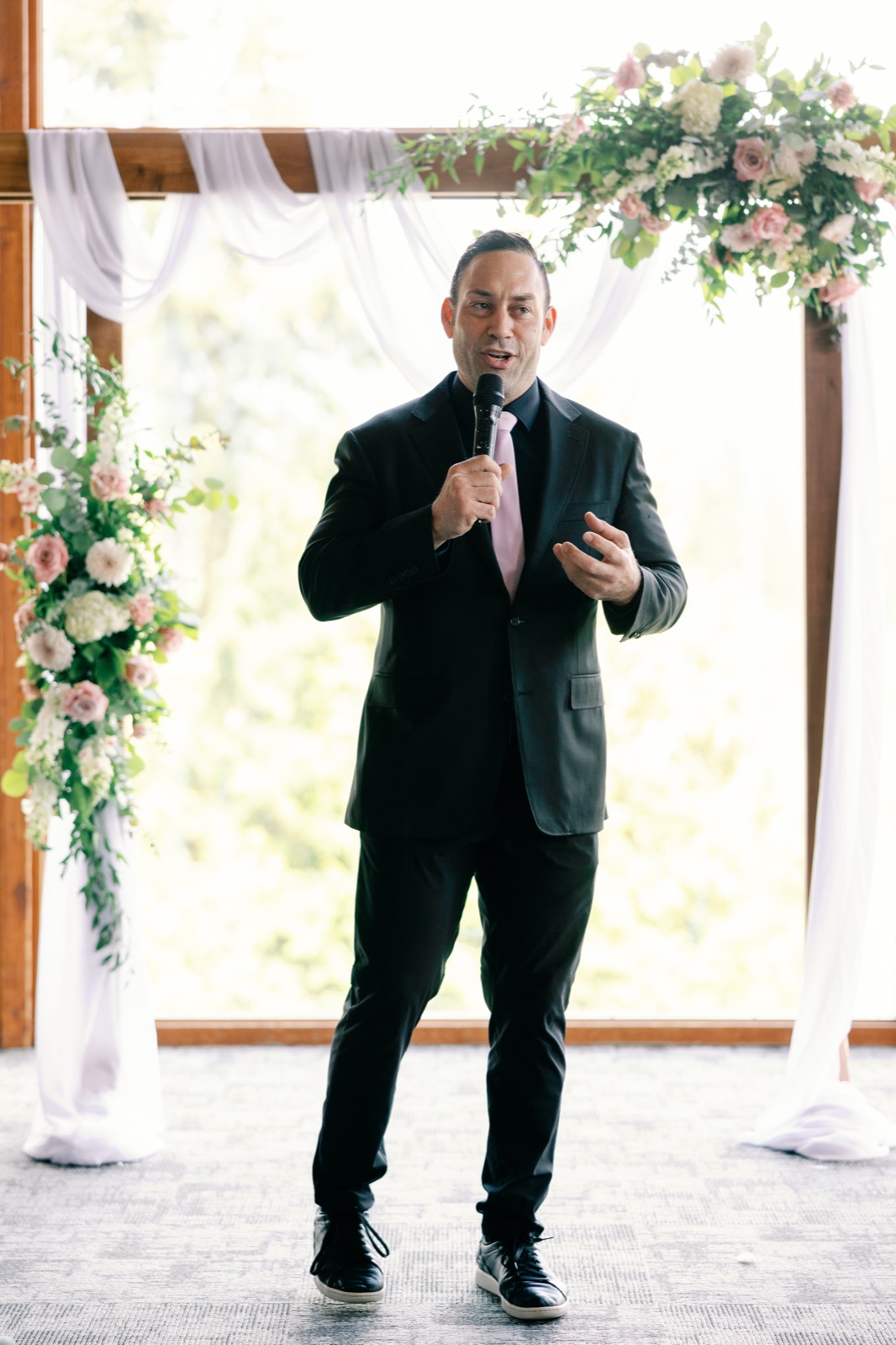 Vancouver MC hosting a wedding ceremony beneath a floral arch