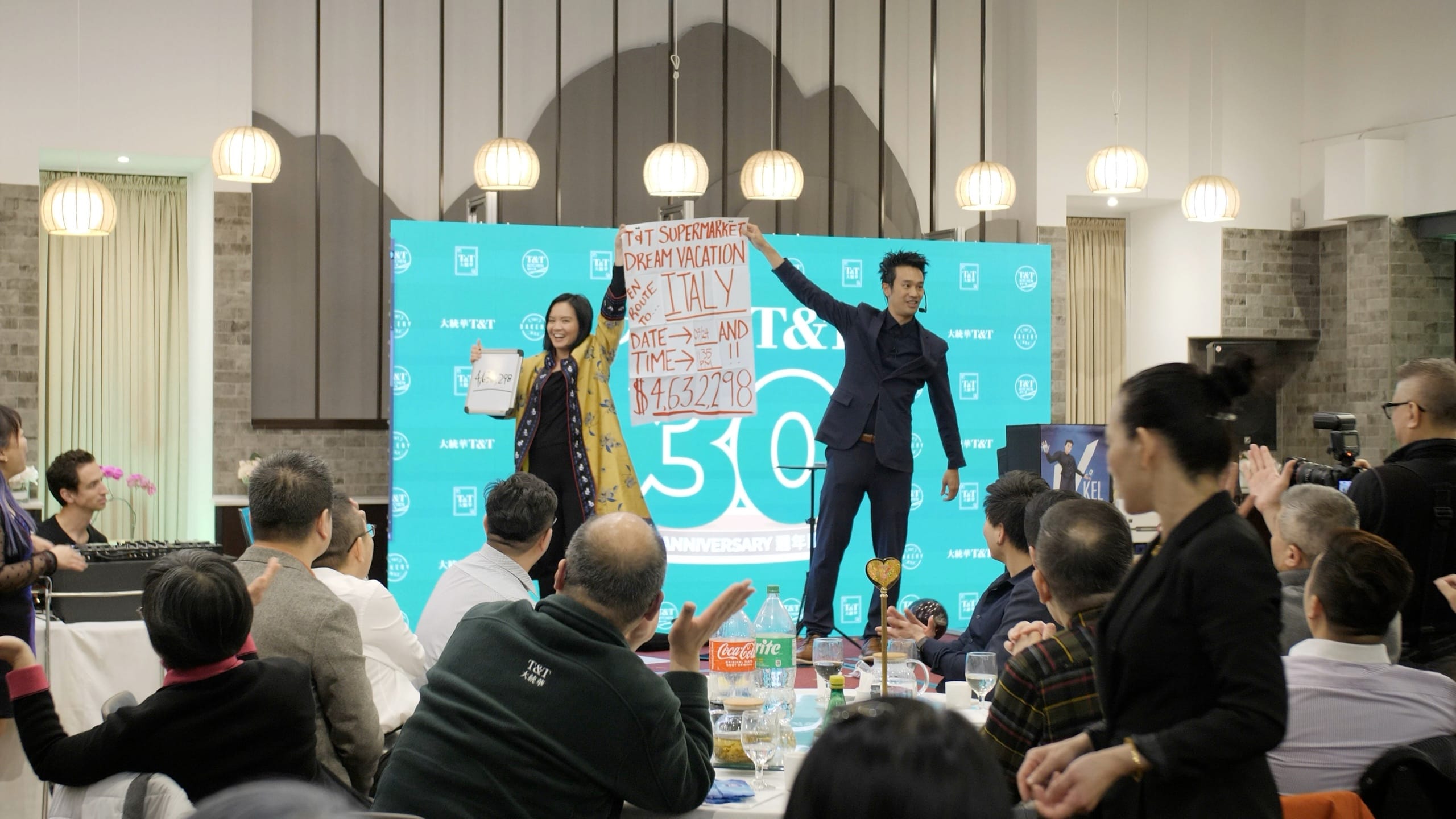 Kel revealing a prediction on stage at T&T Supermarket's 30th anniversary event in Vancouver, crowd applauding