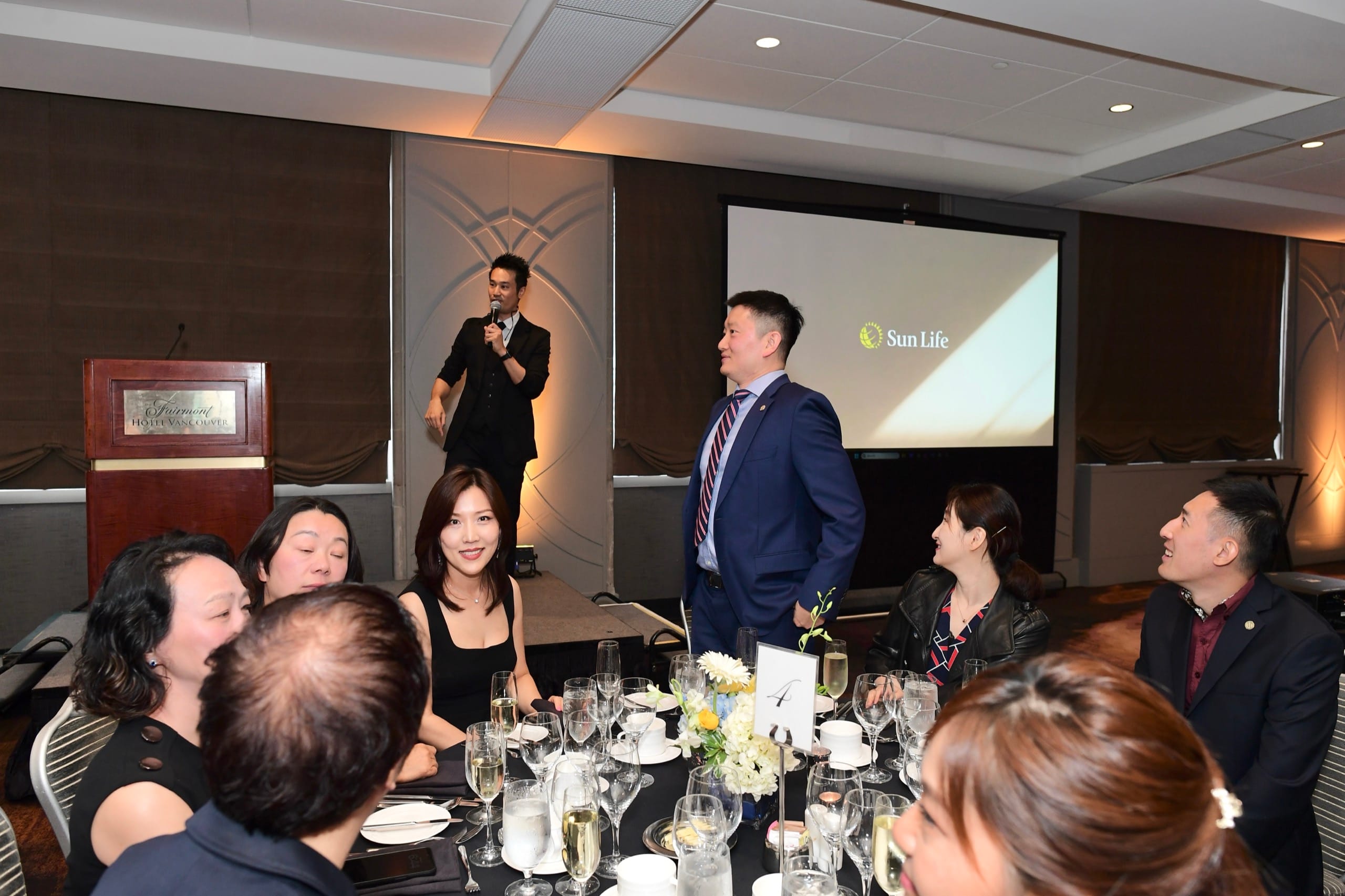 Kel hosting a Vancouver corporate event from a low riser with a microphone in hand