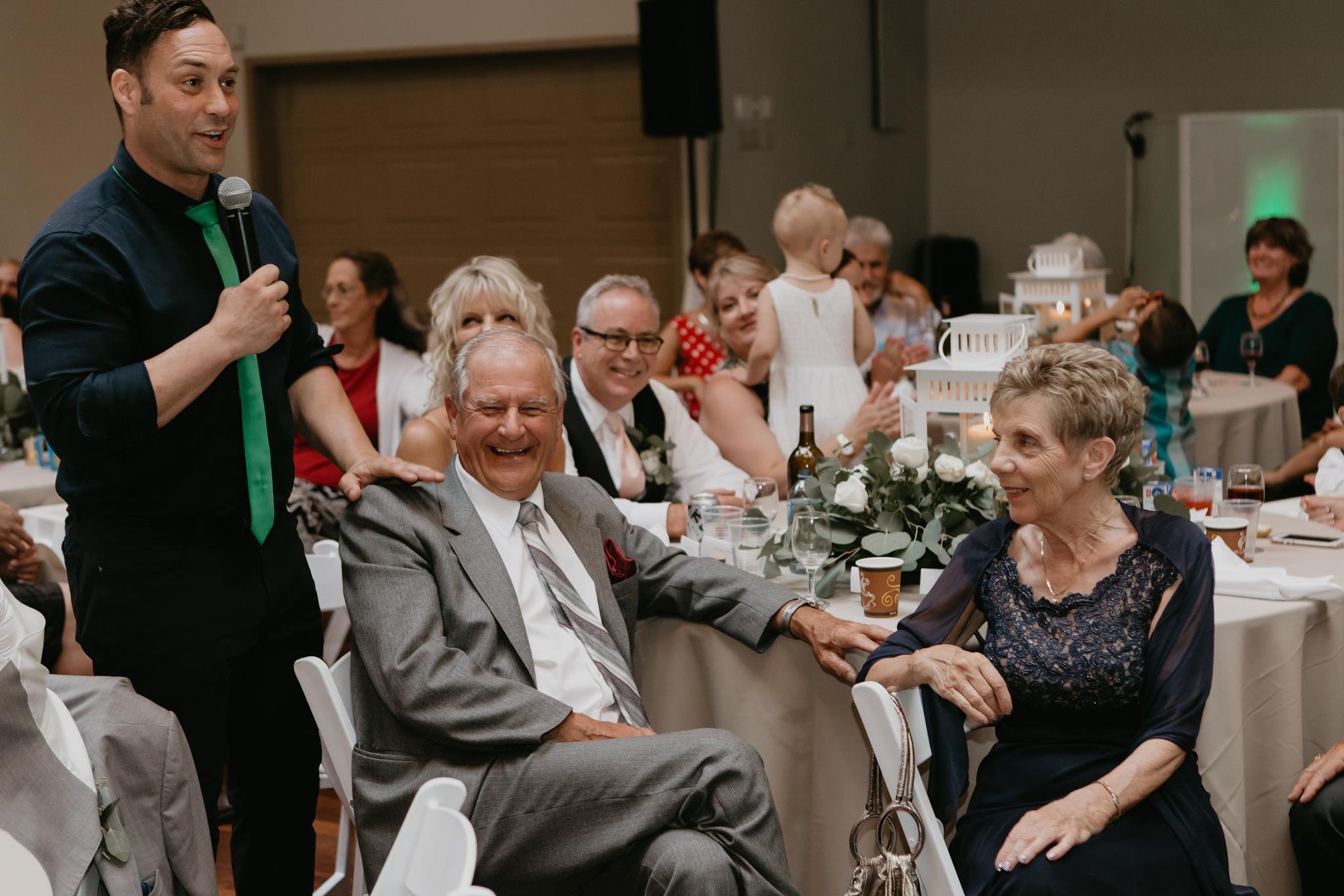 Mike Oulton working a table with a microphone as the whole table laughs at a company Christmas party
